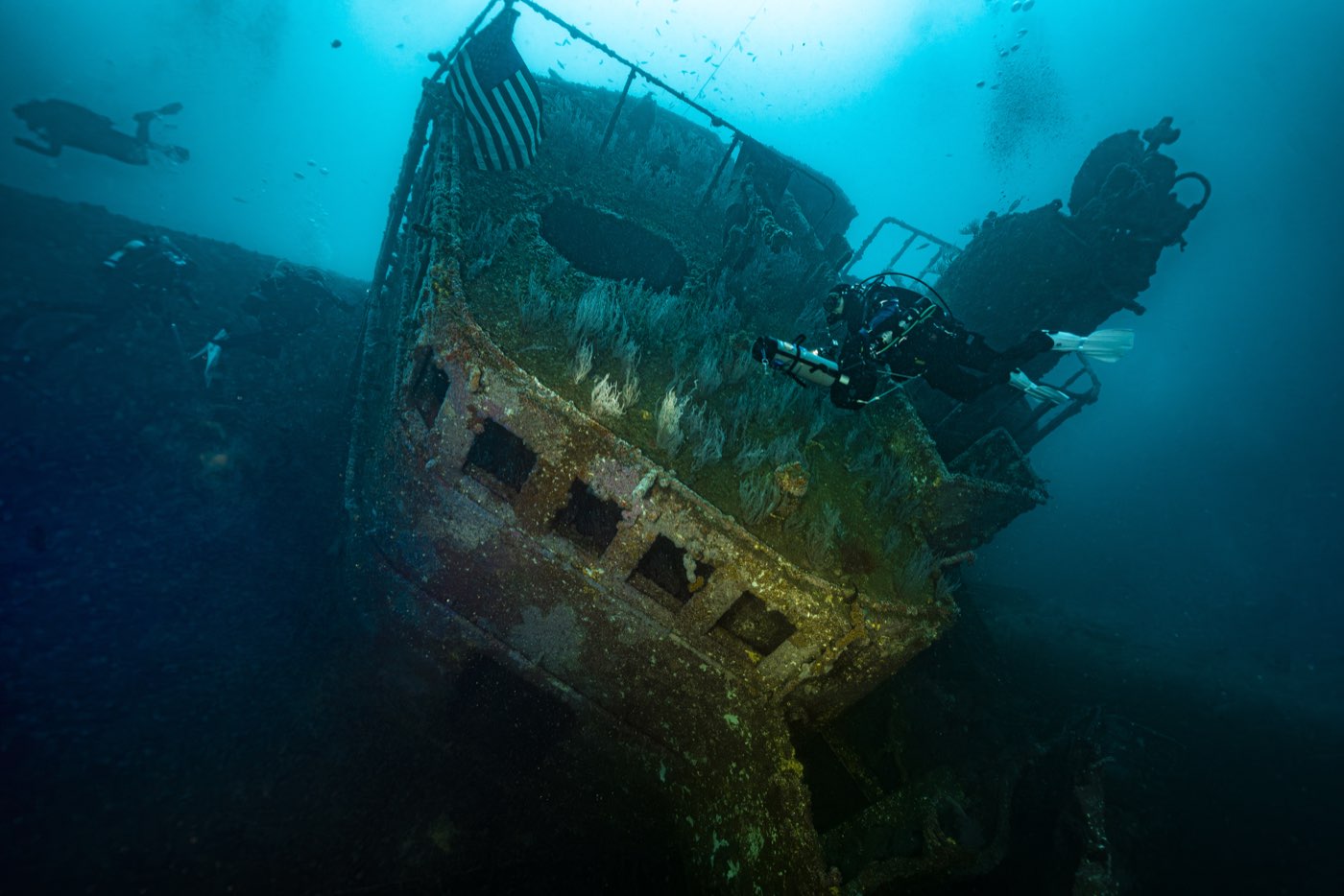 The bridge superstructure, the shallowest part of the wreck, with a flag hung from its rail and a diver alongside